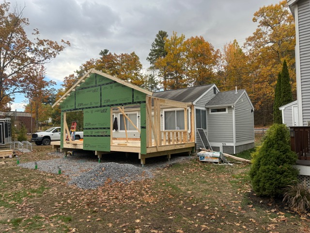 Roof replacement project in progress on a two-story house with roofing materials and equipment on the ground