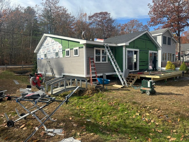 Two-story house undergoing roof repairs with ladders positioned along the roofline and workers on the roof